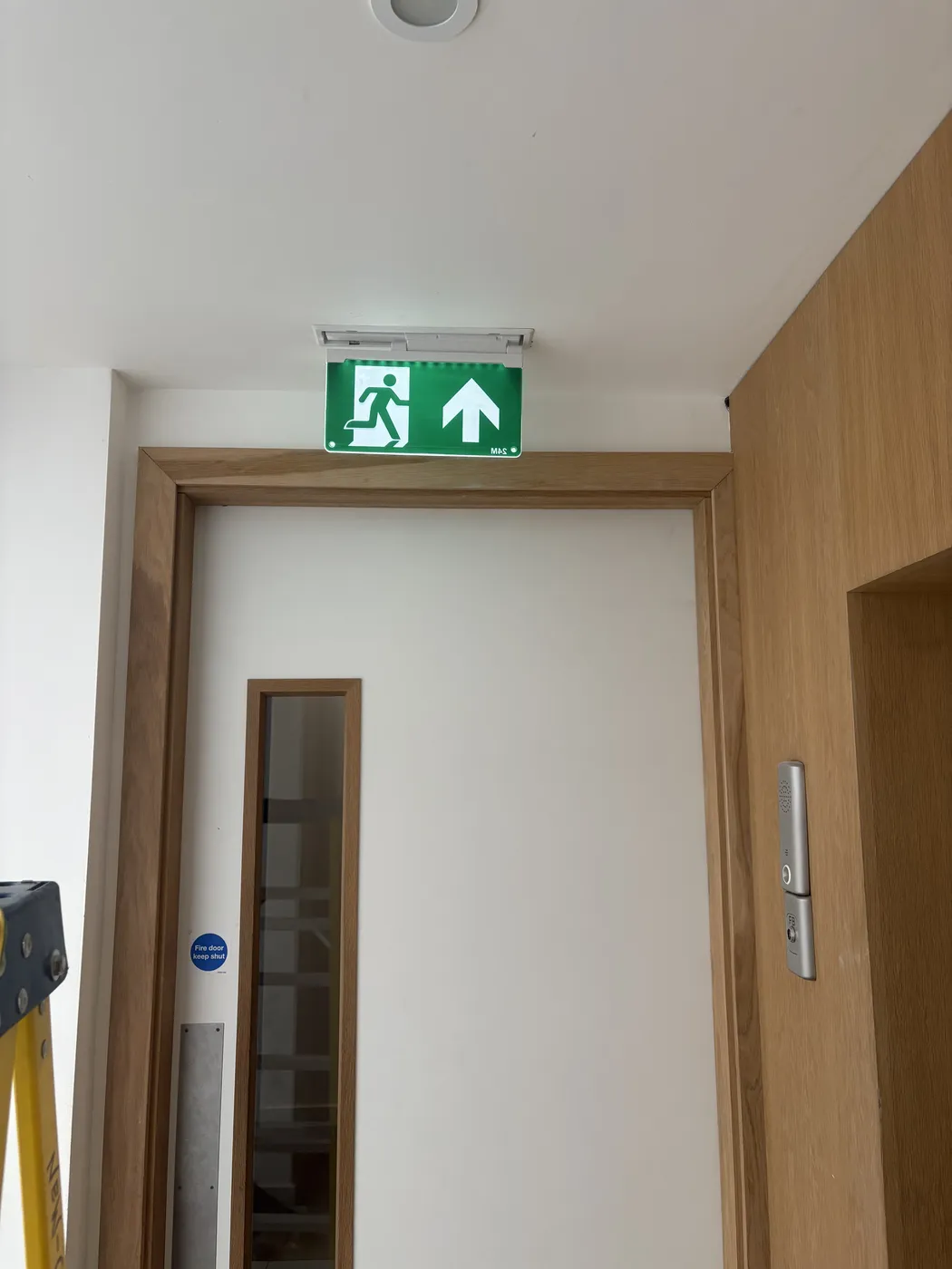 Illuminated emergency exit sign installed above a fire door in Hammersmith