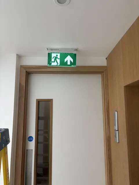 Illuminated emergency exit sign installed above a fire door in Hammersmith
