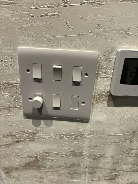 Six-module grid switch with dimmer beside a heating thermostat in Maida Vale